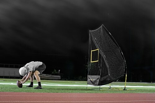 Football player practicing with a training net on a field at night.